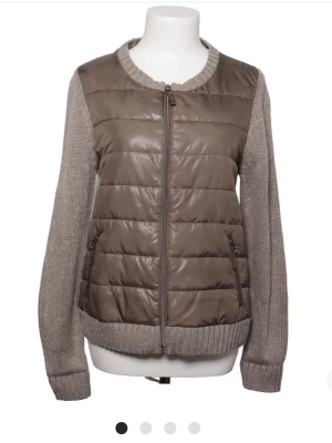 Beige quiltad cardigan med stickade ärmar - Snygg beige cardiganjacka med quiltad framsida och stickade ärmar samt rygg. Jag säljer för den är för stor för mig. Storlek 38. Den är brun/grå