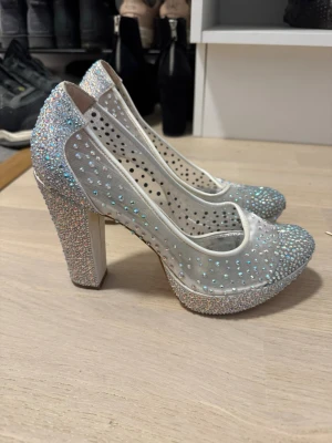 Glittriga pumps med platå och mesh - Snygga pumps med hög klack och platå, täckta av glittrande strass och transparent mesh. Skorna är vita med skimrande detaljer och har en rundad tå. Perfekta för dig som vill sticka ut med extra bling och cool design.