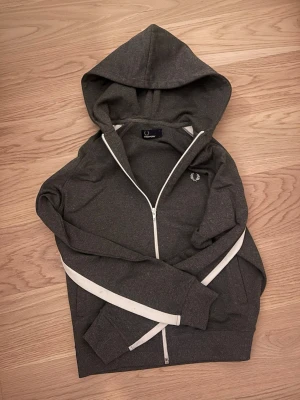 Mörkgrå hoodie från Fred Perry - Jag säljer en grå fredperry hoodie som har storleken xs/s  Hoodien är i mycket bra skick och är ute för ett dunder pris! Jag säljer den för 199kr när den som ny kostar 500kr. Hör av dig vid minsta fråga!
