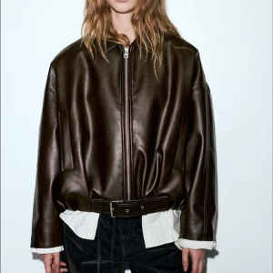 Brun bomberjacka - Snygg oversized skinnjacka från Pull&Bear i mörkbrunt konstläder. Jackan har dragkedja framtill, klassisk krage och ett brett bälte i midjan. Långa ärmar och minimalistisk design ger en cool och modern look. Använd endast 1 gång 💕