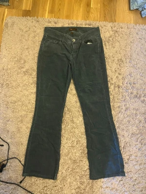 Grå manchesterbyxor från Lee - Snygga grå manchesterbyxor från Lee med bootcut passform och låg midja. Klassisk femficksmodell med dragkedja och knapp framtill. Perfekta för dig som gillar retrostil och vill ha ett par bekväma byxor i mjukt manchestertyg.