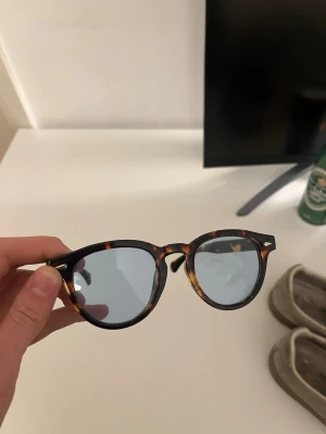 Solglasögon med blått ljus - Snygga solglasögon med runda bågar i klassiskt sköldpaddsmönster och blåtonade glas. Perfekt accessoar för att lyfta din stil under soliga dagar. Bågarna har en tidlös look som passar till det mesta.