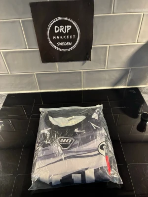 Jul T-shirt  - Säljer en unik limiterad sporttröja från den franska hip hop rapparen jul. den här ett grafiskt mönster i vitt, grått, rött och gult. Tröjan har rund hals, korta ärmar och tryck på bröstet. Perfekt för träning eller match. Materialet känns som funktionsmaterial som andas.