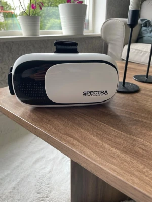 Svartvita VR-glasögon Spectra - Säljer ett par VR-glasögon från Spectra i svart och vitt. De har justerbart band och är tillverkade i plast med mjuk vaddering runt ögonen för extra komfort. Perfekta för att uppleva VR-spel och videos på ett smidigt sätt.