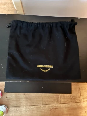 Zadig & Voltaire svart axelväska - Snygg svart axelväska i äkta läder från Zadig & Voltaire med silverfärgade detaljer, kedjerem och ikoniska vingar framtill. Väskan har en praktisk ytterficka med dragkedja och levereras med original dustbag.