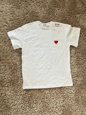 Vit Comme des Garçons Play t-shirt - Vit t-shirt från Comme des Garçons Play med det ikoniska röda hjärtat med ögon broderat på bröstet. Klassisk rund hals och korta ärmar. Perfekt basic med en twist, tillverkad i mjuk bomull.