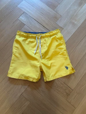 U.S polo Assn badbyxor - Snygga gula badbyxor från U.S polo Assn med elastisk midja och vit snörning. Liten broderad logga framtill och ficka bak. Perfekta för stranden eller poolen. Lätta och snabbtorkande i material som känns bekvämt hela dagen.