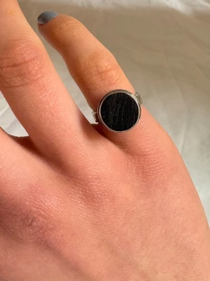 Silverring med svart rund sten - Snygg silverring med en stor, rund svart sten i mitten. Ringen har en enkel och stilren design som passar perfekt för dig som gillar minimalistiska smycken. Metallfärgad ring med slät yta och markerad kontrast mellan silver och svart.