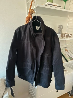 Arket overshirt  - Stilren svart overshirt med klassisk krage och stora fickor framtill. Jackan har knäppning med knappar och är tillverkad i ett kraftigare bomullstyg. Perfekt för lager-på-lager och enkel att matcha med olika outfits.