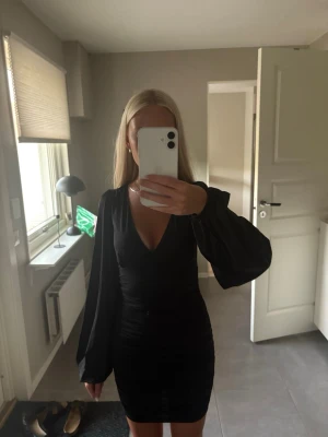 Svart kort klänning  - Snygg svart kort klänning med v-ringning. Klänningen har långa, vida ärmar. 
