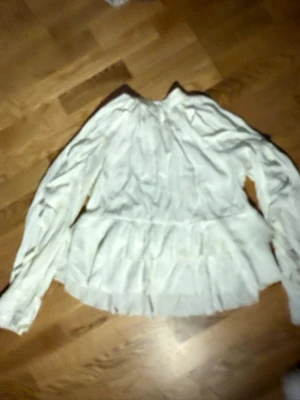 Vit volangblus med lång ärm - Säljer en vit blus med volangdetaljer och rund hals. Blusen har långa ärmar och ett luftigt, flowy tyg som ger en romantisk vibe. Perfekt att styla med jeans eller kjol för en trendig look.