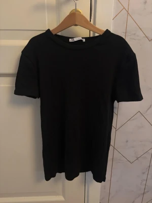 Svart basic t-shirt från Zara - En stilren svart t-shirt från Zara med klassisk passform och rund halsringning. T-shirten är kortärmad och perfekt för en enkel och clean look.