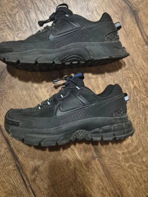 Svarya Nike Zoom Vomero Roam i bra skick - Säljer ett par helsvarta Nike sneakers med robust, chunky sula och detaljer i både mocka och mesh. Skorna har en sportig look med reflekterande detaljer på hälen och snörning med snabblås. Perfekta för dig som gillar streetwear och vill ha något som sticker ut. Skorna är i väldigt bra skick då de bara är anvönda ett fåtal gånger