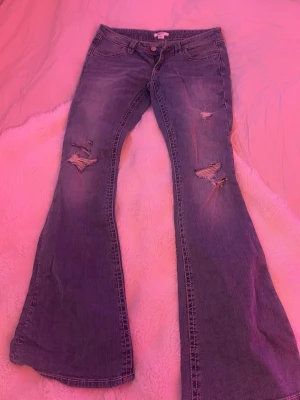 Blå bootcut jeans med slitningar - Säljer ett par blå bootcut jeans med slitna detaljer på låren och knäna samt detaljer på bakfickorna. 