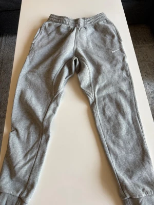 Gråa mjukisbyxor från Nike stl S - Säljer ett par klassiska gråa mjukisbyxor från Nike med resår i midjan och muddar vid bensluten. 