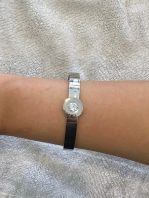 Silverfärgat armband med stor kristall - Snyggt och stilrent armband i silverfärgad metall med en rund, glittrande kristall i mitten från lenmer. Armbandet har en modern och minimalistisk design som passar perfekt till dig som gillar att sticka ut med enkla detaljer. Armbandet är 18cm i omkrets! Aldrig använd. OBS: FRAKTAR INOM 24H!🩷