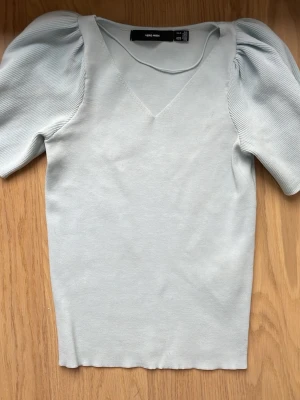 Ljusblå topp med puffärmar  - Supersöt ljusblå topp med v-ringning och trendiga puffärmar. Toppen är ribbad på ärmarna och har en figurnära passform. Perfekt att styla med jeans eller kjol nu under sommaren. 
