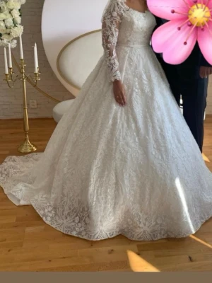 Vit långklänning med spetsdetaljer - Elegant vit långklänning med vackra spetsdetaljer och långärmade spetsärmar. Klänningen har en vid kjol och markerad midja, perfekt för speciella tillfällen. Spetsen ger en romantisk och lyxig känsla. Har använts en gång köpte för 30 000😊 pris kan diskuteras