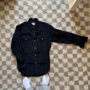 Svart manchesterskjorta från Levi's S - Säljer en svart manchesterskjorta från Levi's i storlek S. Skjortan har klassisk westernstil med två bröstfickor och tryckknappar. Skjortan är lång i modellen.