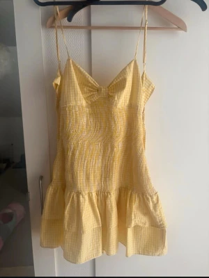 Gul rutig klänning från Zara - Supersöt gul och vit rutig klänning från Zara med smala axelband och volang nertill. Klänningen har en lätt v-ringning och är perfekt för varma dagar. Tillverkad i bomull för en skön och luftig känsla.