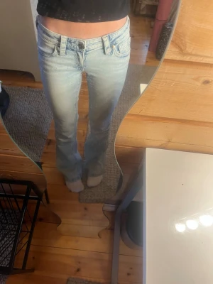 Ljusblå bootcut jeans från Gina Tricot  - Säljer ett par ljusblå bootcut jeans från Gina Tricot Young  med klassisk W-broderad bakficka. Jeansen har låg midja och är tillverkade i mjuk denim med lätt tvättad look. Perfekta för en avslappnad och trendig stil.