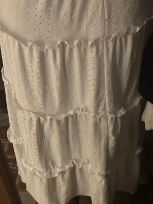 Vit volangkjol med broderade detaljer - Säljer en vit kjol med flera volanger och broderade detaljer. Kjolen har ett romantiskt uttryck med fina hålmönster och mjuka rynkade partier. Perfekt för dig som gillar en feminin och luftig stil.