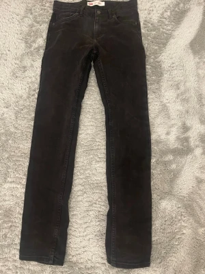Svarta skinny jeans från Levi's - Säljer ett par svarta skinny jeans från Levi's med klassisk femficksdesign och röd logotagg på bakfickan. Jeansen har smal passform och raka ben, perfekta till en avslappnad streetstil.