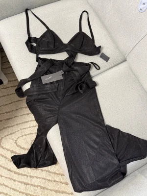 Svart glittrande set  - Snyggt svart set från Relavi med glittrande material. Setet består av en bralette med smala axelband och matchande byxa med hög midja och utsvängda ben. Perfekt för dig som vill sticka ut med en trendig look.