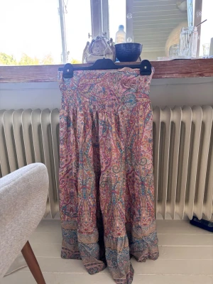 Färgglad långkjol  - Långkjol med färgstarkt i rosa, blått, gult och lila. Kjolen har smock i midjan för skön passform och är tillverkad i ett lätt, luftigt material som passar perfekt till varmare dagar.