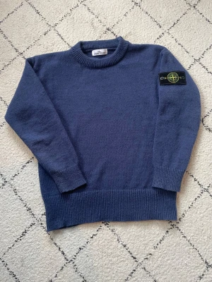 Stone Island - stickad tröja  - Snygg blå stickad tröja från Stone Island med klassisk patch på vänster ärm. Tröjan har rund halsringning, ribbade muddar och nederkant. Perfekt för dig som gillar streetwear och vill ha något stilrent och bekvämt. Tveka inte att höra av dig vid frågor 😊