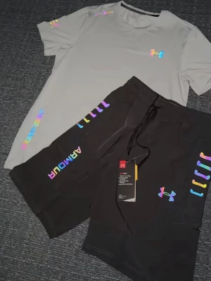 Grå träningsset från Under Armour - Säljer en snygg grå träningsset från Under Armour med färgglada loggor och detaljer längs sidan. Shortsen har snörning i midjan för skön passform och är perfekta för en sportig look. Materialet känns lätt och andas bra. Storlek S, helt ny 
