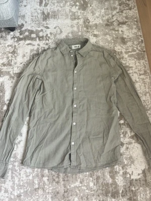 Grön långärmad linneskjorta från Solid - Stilren grön linneskjorta från Solid med klassisk krage och vita knappar framtill. Skjortan är långärmad och har en avslappnad passform, perfekt till jeans eller chinos. Tillverkad i mjuk bomull för skön känsla hela dagen.