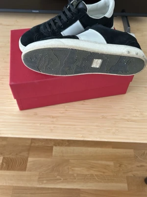 Valentino Garavani svarta sneakers - Snygga sneakers från Valentino Garavani i svart mocka med vita detaljer och vit sula. Klassisk låg modell med svart snörning och logga på plösen. Perfekta för dig som vill ha en stilren och exklusiv look.