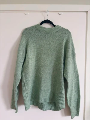 Ljusgrön oversized stickad tröja - Mysig ljusgrön stickad tröja med avslappnad passform och rund hals. Tröjan har långa ärmar och ribbade muddar vid ärmslut och nederkant. 