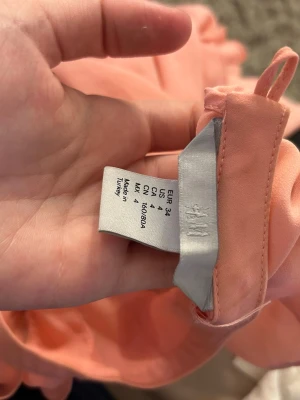 Rosa ärmlös blus från H&M, köpt secondhand  - Söt rosa blus från H&M i storlek 34. Blusen är ärmlös och har volangdetaljer framtill som ger en romantisk och trendig look. Tillverkad i ett lätt och luftigt material, perfekt för varma dagar eller lager på lager.