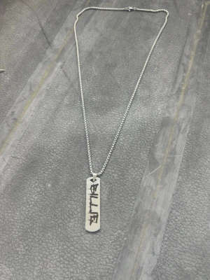 Billie Eilish Silverfärgat halsband med bricka - Billie Eilish Snyggt halsband i silverfärg med en rektangulär bricka som har ingraverad text i svart. Kedjan är tunn och stilren, och brickan ger en cool och personlig touch till din outfit. Perfekt accessoar för dig som gillar minimalistisk och modern stil.
