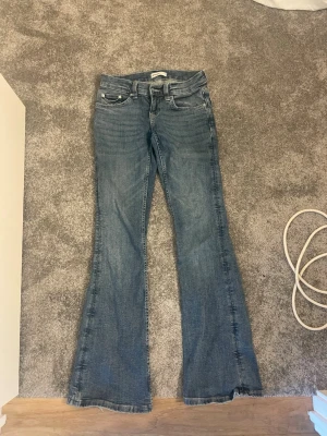 Blå bootcut jeans med fickdetaljer - Säljer ett par blå bootcut jeans med klassisk femficksdesign och snygga sömmar på bakfickorna. Jeansen har normal midja och är tillverkade i ett mjukt denimtyg. Perfekta för dig som gillar en retroinspirerad look med utsvängda ben.
