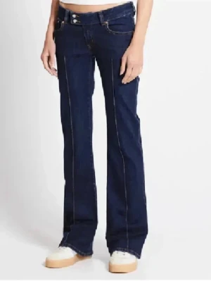 Mörkblå bootcut jeans med kontrastsömmar - Säljer ett par mörkblå bootcut jeans med snygga kontrastsömmar längs benen och klassiska fem fickor. Jeansen har hög midja och stängs med knapp och dragkedja. Perfekta för dig som gillar en retroinspirerad look.