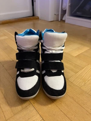 Svarta och vita wedge sneakers från Sugar - Snygga wedge sneakers från Sugar i svart och vitt med blått foder. Skorna har perforerat läder, mockadetaljer och tre breda kardborreband. Högt skaft och cool design som sticker ut.