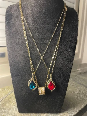 Tre Guldhalsband med blå och röd sten pläterade i guld 18k - Tre eleganta guldhalsband med droppformade hängen, ett med blå sten och ett med röd sten, samt ett med fin zirkonhängare. Alla är i Copper ( rostfritt) och pläterade i guld 18k. Perfekt för att ge din outfit extra bling.