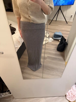 Grå ribbad långkjol i stickat material - Snygg grå långkjol i ribbstickat material med hög midja. Kjolen har en figurnära passform och är perfekt för dig som gillar en stilren och enkel look. Passar till både stickade tröjor och crop tops.