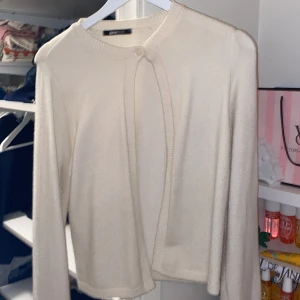 Krämvit kofta från Gina Tricot - Snygg krämvit kofta från Gina Tricot med rund halsringning och knapp framtill. Koftan har långa ärmar och ribbade kanter. Perfekt att slänga över en topp för en stilren look.