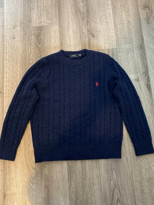 Mörkblå kabelstickad tröja Polo Ralph Lauren - Säljer en stickad tröja från Polo Ralph Lauren, då den börjar bli för liten för mig. Perfekt för dig som gillar tidlös och stilren design. Storlek M men liten i storlek så passar nog S också.