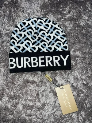 Mössor - Säljer en snygg mössa från hm med svart och vit logotypmönster samt stor text framtill. Mössan är stickad och har en uppvikt kant. Perfekt för dig som vill ha en trendig accessoar med lyxig känsla.