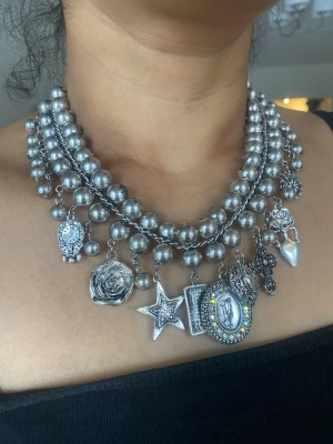 Chunky silverfärgat pärlhalsband med berlocker - Stilrent halsband i silverfärg med stora pärlor i flera rader och unika berlocker som stjärna, ros, hjärta och medaljong. Statement piece som drar blickarna till sig och passar perfekt till en edgy look.