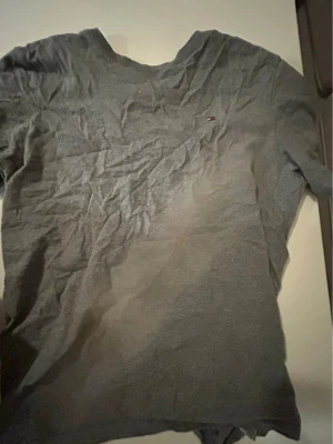 Grå t-shirt från Tommy Hilfiger - En enkel grå t-shirt från Tommy Hilfiger med liten logga på bröstet. Klassisk passform och rund halsringning. Perfekt basplagg till garderoben och lätt att matcha med andra plagg.