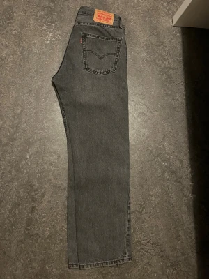 Svarta Levi's 501 raka jeans - Klassiska svarta Levi's 501 jeans med rak passform och fem fickor. Jeansen har en vintage-vibe med knappgylf och ikonisk läderpatch bak i midjan. Tillverkade i slitstark bomullsdenim. Perfekta för en avslappnad och tidlös stil.
