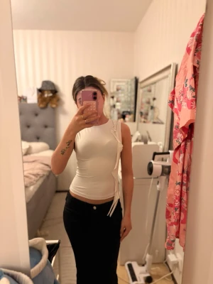 Vit ärmlös topp med volang - Snygg vit kortärmad topp med volang på sidan. Toppens design är slim och den har en enkel, modern look som passar perfekt till jeans eller kjol. Materialet känns mjukt och stretchigt, vilket gör den bekväm att bära.