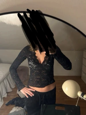 Svart spetsblus med v-ringning - Säljer en svart långärmad blus i genombruten spets med djup v-ringning och fina spetsdetaljer. Toppen är figurnära och har transparent material som ger en trendig look. Perfekt att styla med höga byxor eller kjol. Använd 1 gång 