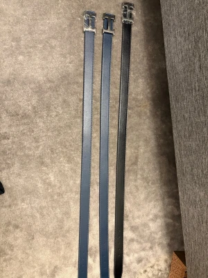 Svart och blått skärp med silverdetaljer - Säljer tre stilrena bälten i svart och blått med silverfärgade spännen. Bältena är smala och har en klassisk design som passar till jeans eller kostymbyxor. Tillverkade i präglat skinn för en exklusiv känsla.